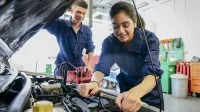 Auszubildende für Kraftfahrzeugmechatronik bei der Arbeit am Auto in der Werkstatt
