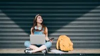 junge Frau im Schneidersitz mit Laptop und Smartphone