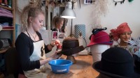 Eine Modistin bügelt eine Hutkrempe in einem Atelier.