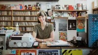 Eine Musikfachhändlerin steht im Plattenladen hinter der Verkaufstheke.