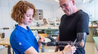 Eine Orthopädietechnik-Mechanikerin passt eine Armprothese an einem Patienten an.