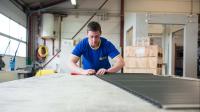 Ein Rollladen- und Sonnenschutzmechatroniker repariert in der Werkstatt einen Rollladen.
