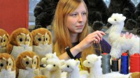 Eine Spielzeugherstellerin kämmt in der Werkstatt die neu hergestellten Alpakas und Eulen aus Plüsch.