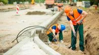 Ein Straßenbauer schaufelt Sand an den Straßenrand für einen neuen Gehweg.
