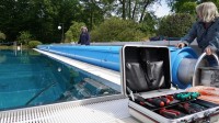Zwei Technische Konfektionäre installieren die Abdeckplane für das 50-Meter-Becken eines Freibads.