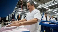Ein Textilreiniger bügelt Kleidung mit einer Dampfbügelmaschine.
