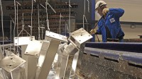 Ein Verfahrensmechaniker entfernt Asche und Restbestände bei der Verzinkung von Stahlteilen im Zinkkessel.