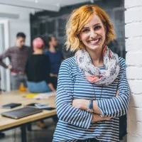 Eine junge Lehrerin steht in einem Klassenzimmer, im Hintergrund sind weitere Lehrkräfte zu sehen