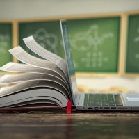 Eine Mischung aus Buch und Laptop vor einer Tafel