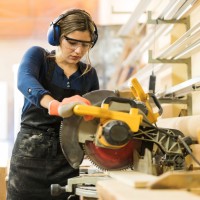 Eine junge Frau arbeitet an einer Kreissäge in einem holzverarbeitenden Betrieb.