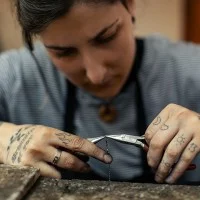 Eine tätowierte Gold- und Silberschmiedin arbeitet an einer Kette.