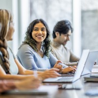 Drei Frauen und ein Mann sitzen vor ihren Laptops und lernen.