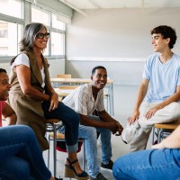 Ein Klassenraum,  in dem eine Lehrerin mit sechs Lernenden im lockeren Stuhlkreis sitzt.