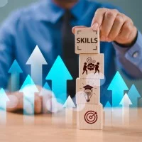 Tisch mit einem Stapel Holzwürfel, auf denen Symbole aus dem Bereich Lernen abgebildet sind. Im Hintergrund ein Anzugträger, der mit seiner Hand die Würfel stapelt. Viele blaue und weiße Pfeile zeigen im Bild nach oben