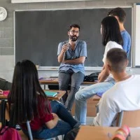 Ein Berufsschullehrer lehnt am Pult und diskutiert mit einigen Schülerinnen und Schülern.