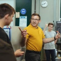 Ein Lehrer und drei Auszubildende stehen vor Maschinen und diskutieren.