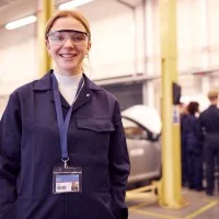 Junge Frau mit anderen Auszubildenden in einer Autowerkstatt