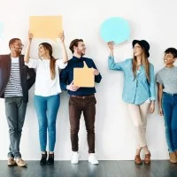 Fünf junge, fröhliche Menschen lehnen an einer Wand halten Sprechblasen aus Papier hoch.