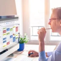 Eine Frau organisiert Termine, Aufgaben und Arbeitszeiten am Computer mit einem digitalen Kalender.