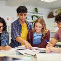 Fünf Schülerinnen und Schüler arbeiten zusammen an einem Tisch mit Heften und Büchern.