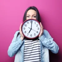 Eine Frau hält eine große runde Uhr vor sich.