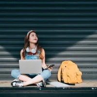 junge Frau im Schneidersitz mit Laptop und Smartphone