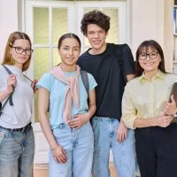 Zwei Schülerinnen, ein Schüler und eine Lehrerin stehen in der Bibliothek und lächeln in die Kamera.