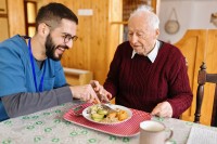 Ein Altenpfleger unterstützt einen Senior beim Mittagsessen.