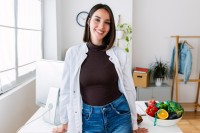 Eine Frau in einem weißen Kittel steht an einem Schreibtisch, auf dem eine Schüssel mit frischem Obst und Gemüse platziert ist.