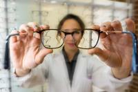 Eine Augenoptikerin reicht einem Kunden seine neue Brille zur Anprobe.
