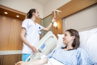 Eine Gesundheits- und Krankenpflegerin überprüft die Einstellung des Tropfes einer Patientin, die im Krankenbett liegt.