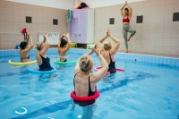 Eine Masseurin und medizinische Bademeisterin trainiert eine Gruppe Senioren in einem Wasserbecken. 