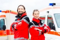 Ein Rettungssanitäterteam in roter Uniform steht vor zwei Krankenwägen, bereit für den nächsten Einsatz.