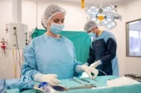 Eine operationstechnische Assistentin in OP-Kleidung richtet Instrumente auf einem Tisch für eine bevorstehende Operation her. Im Hintergrund arbeitet ebenfalls ein operationstechnischer Assistent.