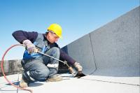 Ein Bauwerksabdichter bringt Dachpappe durch Erhitzen mit einem Gasbrenner auf einem Flachdach an. 