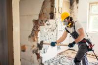 Ein Bauwerksmechaniker für Abbruch und Betontrenntechnik schlägt mit einem Hammer eine Wand in einem Wohngebäude ein.