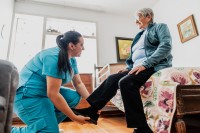 Eine Pflegefachfrau unterstützt während eines Hausbesuchs eine Seniorin beim Anziehen.