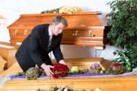 Eine Bestattungsfachkraft schmückt einen Sarg mit Blumengebinden.