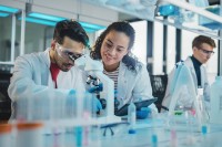 Eine biologisch-technische Assistentin unterstützt einen Naturwissenschaftler beim Mikroskopieren und Dokumentieren der Ergebnisse.