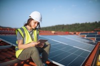 Eine technische Assistentin für regenerative Energietechnik überprüft an ihrem Tablet die richtige Einstellung der Photovoltaik-Anlage.