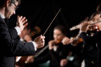 Ein Ensembleleiter hält einen Taktstock, mit dem er ein Orchester anleitet. 