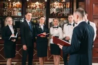 Ein Assistent für Hotelmanagement und sein Team aus sechs Mitarbeitenden stehen im Festsaal und besprechen das Menü à la carte.