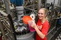 Eine Chemikantin füllt eine Flüssigkeit in eine Maschine für Waschmittelproduktion.