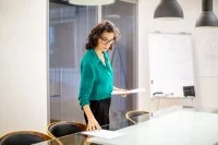 Eine kaufmännische Assistentin / Wirtschaftsassistentin platziert Dokumente auf den Tisch im Besprechungsraum.