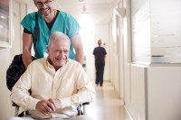 Ein Gesundheits- und Krankenpflegehelfer bringt einen entlassenen Patienten mit dem Rollstuhl zum Ausgang des Krankenhaus.
