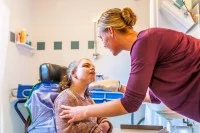 Eine Pflegeassistentin wäscht im Badezimmer ein körperlich eingeschränktes Mädchen, das im Rollstuhl sitzt, mit einem Waschlappen.