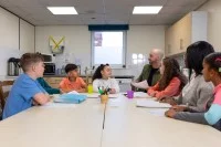 Ein Sozialassistent kümmert sich in einer Gemeinschaftsküche um eine Gruppe Kinder verschiedener ethnischer Herkunft. 