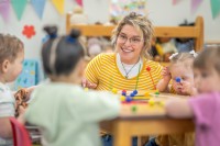 Eine sozialpädagogische Assistentin/ Kinderpflegerin spielt mit einer Kleinkindergruppe in einem Kinderhort.