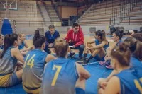 Ein Sportassistent und ein Trainiersitzen mit ihrer Mannschaft auf dem Boden der Sporthalle und besprechen.