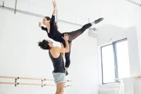 Eine Bühnentänzer hebt ein Bühnentänzerin im Proberaum mit seinen Händen hoch. 